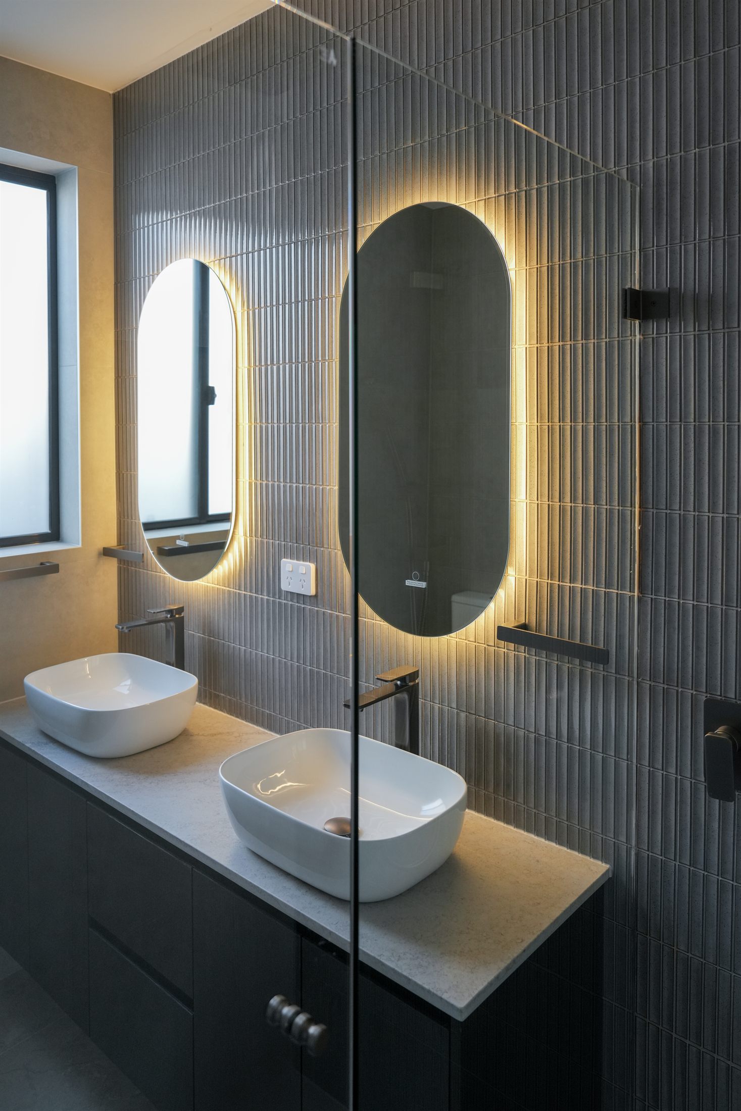 Ensuite with double vanity, backlit oval mirrors and grey finger tiles in one of the dual-occupancy homes in Sydney's North West
